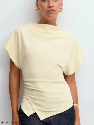 Gina Tricot butter yellow asymmetrisk topp – strl S – knappt använd - Snygg ljusgul topp med omlottdetalj i midjan och korta ärmar. Toppen har en asymmetrisk nederkant och en mjuk, följsam passform som ger en modern siluett. Perfekt att styla med jeans eller kjol för en trendig look.
