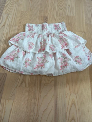 Vit blommig volangkjol - Söt kort kjol från Kappahl l i vitt med rosa blommönster och bred smock i midjan. Kjolen har dubbla volanger som ger en romantisk och luftig känsla. Perfekt för vår och sommar, till både sneakers och sandaler. Super fin och somrig! Använd men har inga tecken på användning?