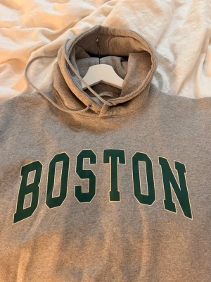 Grå oversized Hoodie med BOSTON-tryck - Snygg grå hoodie med stor grön BOSTON-text på bröstet. 