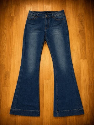 Åhléns bootcut jeans – stl 38 - Märke: Åhléns Storlek: 38 Färg: Mellanblå denim Material: 85 % bomull, 13 % polyester, 2 % elastan Passform: Bootcut / utsvängda ben Skick: Nyskick – endast använda någon enstaka gång.  Mått (platt mätta, ca):  * Midja: 38 cm (ca 76 cm runt om) * Innerbenslängd: 83 cm  Perfekta vardagsjeans med bekväm stretch och en klassisk siluett som aldrig går ur stil.