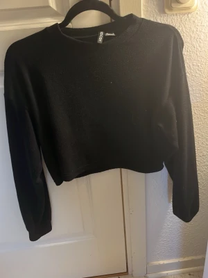 Svart croppad tröja från Divided - En enkel svart croppad tröja från Divided med rund halsringning och långa ärmar. Perfekt till jeans eller kjol för en clean och stilren look. Materialet känns mjukt och bekvämt mot huden.