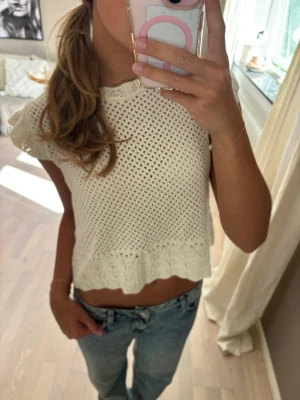 Vit stickad croppad topp - Superfin vit stickad topp med korta ärmar och croppad passform. Toppen har ett luftigt hålmönster och en söt volangkant nedtill. Perfekt för varma dagar och enkel att styla med jeans eller kjol. Helt ny, aldrig använd lapp sitter kvar 