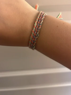Färgglatt flätat vänskapsarmband - Säljer ett handgjort flätat vänskapsarmband i flera färger som rosa, mintgrön, vit och orange. Armbandet är gjort av tunna bomullstrådar och har en enkel knytning. Perfekt accessoar för dig som gillar boho-stil och personliga detaljer.