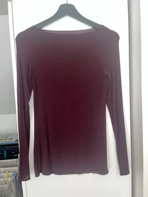 Vinröd långärmad topp - En enkel och stilren vinröd långärmad topp med rund halsringning. Toppen har en slim passform och är tillverkad i ett mjukt, tunt material som känns skönt mot huden. 