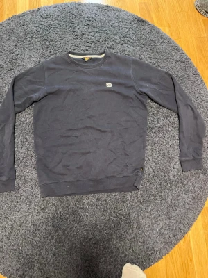 Mörkblå sweatshirt från Lee - Snygg mörkblå sweatshirt från Lee med rund halsringning och diskret logga broderad på bröstet. Tröjan har långa ärmar och ribbade muddar vid ärmslut och nederkant. Perfekt för en avslappnad och stilren look.
