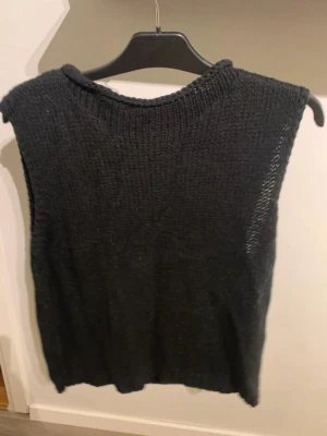 Svart stickad väst från Saint Tropez - Svart stickad väst från Saint Tropez i enkel, rak modell utan ärmar. Perfekt att styla över en skjorta eller t-shirt för en trendig lager-på-lager-look. Mjuk och skön känsla, rund halsringning och diskret struktur i stickningen.