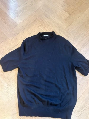 Svart stickad tröja Filippa K - Stickad tröja från Filippa K med halvpolo i mjukt material storlek M.. Både stilren och enkel - något nopprig och en liten fläck vid kragen.