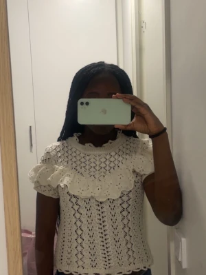 Vit spetsblus med volang - Säljer en söt vit blus med spetsdetaljer och stor volang över bröstet och axlarna. Blusen är kortärmad och har ett romantiskt, luftigt mönster som passar perfekt till jeans eller kjol. Perfekt för dig som gillar en feminin och trendig stil.