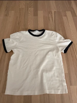 Vit t-shirt från Zara - Klassisk vit t-shirt med svarta muddar vid halsringning och ärmslut. Enkel och stilren design som passar till det mesta. Tillverkad i mjukt material och har en normal passform med korta ärmar.