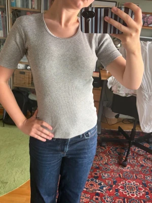 Ljusgrå ribbad topp med kort ärm - Säljer en ljusgrå ribbad topp med rund halsringning och korta ärmar. Toppen har en slim passform och är tillverkad i ett mjukt, stretchigt material som sitter snyggt på kroppen. Perfekt att styla med jeans eller kjol. Hör av dig vid frågor!
