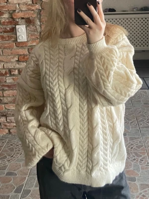 Oversize kabelstickad vit tröja - Säljer en oversize kabelstickad tröja i mjuk cremevit ullblandning. Tröjan har rund halsringning, breda ärmar och ribbade muddar. 
