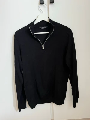 Svart stickad tröja med halvzip - Snygg svart stickad tröja från ONLY & SONS med halvzip och hög krage. Tröjan har långa ärmar och ribbade muddar vid ärmslut och nederkant. 