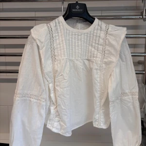 Vit blus med spetsdetaljer - Vit blus med volanger och spets detaljer. Lite kortare i modellen. Storlek S, sitter med som XS. 