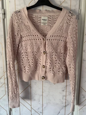 Ljusrosa stickad kofta från Dobber - Viktoria knitted cardigan. Söt ljusrosa stickad kofta från Dobber med v-ringning och dekorativa hålmönster. Koftan har långa ärmar, ribbade muddar och fyra pärlemorskimrande knappar framtill. 