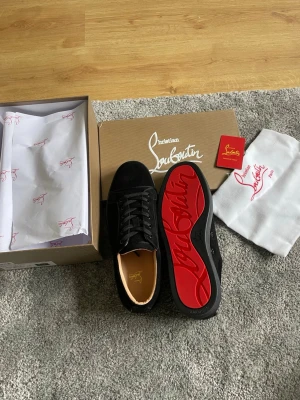 Svarta sneakers från Christian Louboutin - Stilrena svarta sneakers från Christian Louboutin i mocka med klassisk röd sula och svarta skosnören. Insidan är beige och sulan har den ikoniska Louboutin-loggan i rött. Perfekta för dig som vill ha något exklusivt och trendigt. Helt nya aldrig testade eller använda. Alla tillbehör ingår. Pris kan diskuteras vid snabb affär.  43 finns storlek 
