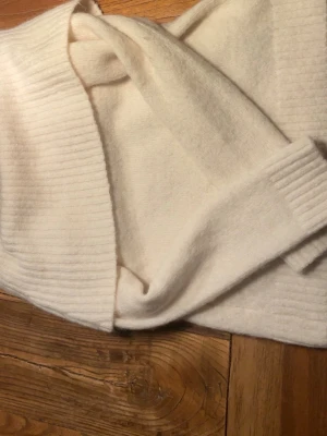 Vit ribbad kofta i mjukt material - Säljer en krämvit kofta med ribbade detaljer längs kanter och ärmslut. Koftan är öppen framtill och har en avslappnad passform, perfekt att slänga på sig över en t-shirt. Materialet känns mjukt och gosigt, perfekt för kyliga dagar.