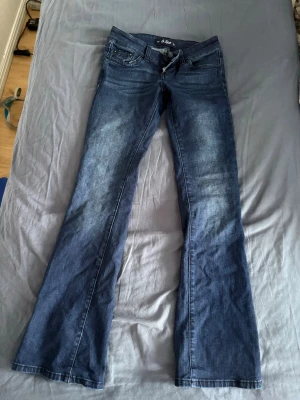 Low rise Mörkblå bootcut jeans från G.Rise - Snygga mörkblå bootcut jeans från G.Rise med klassisk femficksdesign och slitningar framtill. Jeansen har normal midja, dragkedja och knapp i gylfen samt bälteshällor. Perfekta för en avslappnad och trendig look. Mycket low rise, ny skick! Köpte för 1200kr, långa i storleken