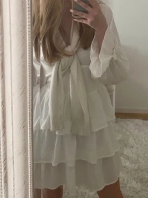 Vit volangklänning från Zara - Supersöt vit kortklänning från Zara med volanger, v-ringning och dekorativa knappar framtill. Klänningen har långa ärmar med volangdetaljer och en romantisk krage med broderad spets. Perfekt för sommarens alla tillfällen!