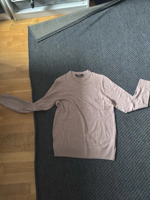Beige stickad tröja från Primark - Stickad tröja i beige från Primark med rund hals och långa ärmar. Tröjan har en enkel och stilren design med ribbstickade muddar vid halsen, ärmslut och nederkant. Perfekt för att hålla sig varm under kyliga dagar.