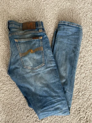 Nudie Jeans - Snygga blå skinny jeans från Nudie Jeans med klassisk femficksmodell och gul söm på bakfickan. Jeansen har en något tvättad look och är tillverkade i mjuk denim. Perfekta för dig som gillar en smal passform och stilren design. Skriv om du har frågor!