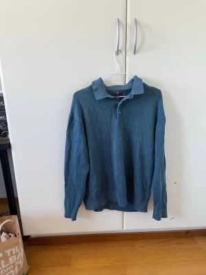 Blå pikétröja med krage - Säljer en stilren blå pikétröja med klassisk krage och knäppning framtill. Tröjan har långa ärmar och ribbade muddar vid ärmslut och nederkant. Perfekt för en avslappnad men ändå snygg look.