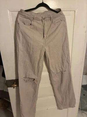 Beige ripped jeans från H&M - Säljer ett par beige jeans från H&M med raka ben och slitningar över knäna. Klassisk femficksmodell med knapp och dragkedja. Materialet är bomull med lite stretch för extra komfort. Perfekta för en avslappnad och trendig look.