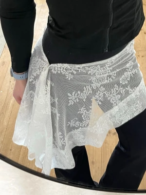 Vit spetskjol med blommigt mönster - Säljer en kort vit handgjord kjol i spets med blommigt mönster och omlott-design. Kjolen är lätt och luftig, perfekt för dig som gillar en romantisk och feminin stil. Passar snyggt över tights eller jeans för en cool look. Passar S/M