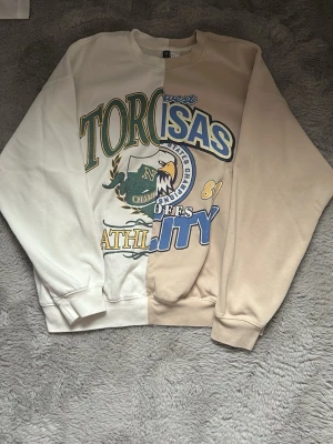 Beige och vit college-tröja - Säljer en unik tvåfärgad college-tröja från H&M, ena sidan beige och andra sidan vit. Framsidan har ett stort tryck. Tröjan har rund halsringning och ribbade muddar. Köpt på hm för ca 2 år sedan och använd 2-3 ggr så jag tycker den är lite för stor för mig. Tröjan i sig är i väldigt bra skick, inga defekter alls. Säljer som sagt då den ej kommer till användning :))