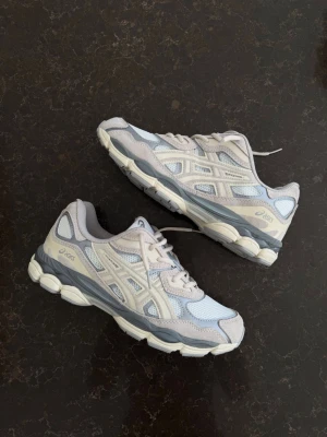 Asics sneakers i beige och grå mesh - Snygga Asics sneakers i beige, grå och vitt med mesh- och mockadetaljer. Skorna har en chunky sula och klassisk Asics-logga på sidan. Perfekta för dig som gillar sportig och trendig stil. Låga och bekväma med snörning.