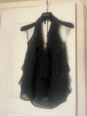 Svart volang topp från Zara - Elegant svart volangtopp från Zara i storlek S. Den är V-ringad och öppen i ryggen. Perfekt till utekvällar, middag eller fest!🌸