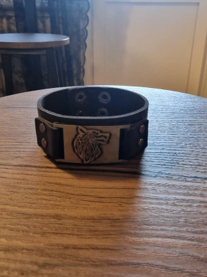 Armband vintage viking varg - Svart läderarmband med ett detaljerat viking varg i metall. Armbandet har justerbara tryckknappar för att passa olika handledsstorlekar. Storlek 23 cm långt. Bredd 3 cm.