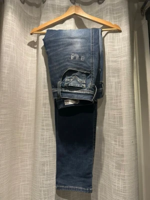 Slitna Replay Jeans - Säljer ett par blå replay jeans med slitningar och broderade detaljer på låret. Jeansen har en smal passform och klassisk femficksdesign. Perfekta för dig som gillar en avslappnad och trendig stil. Modellen är 185 cm 75 kg