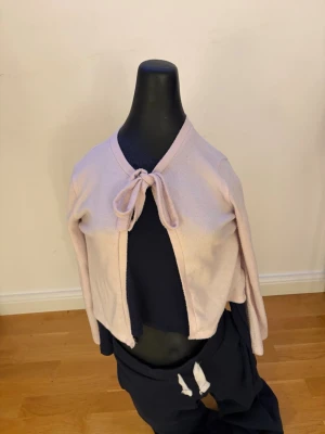 Ljusrosa cropped kofta med knyt - Supersöt ljusrosa cropped kofta med knyt framtill. Koftan har långa ärmar och är gjord i ett mjukt, tunt material som känns skönt mot huden. Perfekt att slänga över ett linne eller t-shirt för en chill och trendig look.