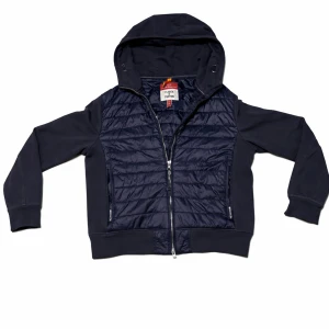 Mörkblå quiltad pufferjacka med huva - Snygg mörkblå cardigan från Parajumpers med quiltad front och rygg, huva och dragkedja framtill. Cardiganen har långa ärmar och ribbade muddar. Perfekt för dig som vill ha en modern look. Den är i bra skick och ny priset är 4499kr priset är ej hugget i sten kan sänka vid snabb affär! Tröjan är barnstorlek XL som motsvarar xxs/xs