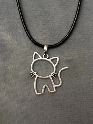 Katt halsband silver imitation  - Snyggt halsband med en berlock i form av en siluett av en katt. Trädd på en svart tråd, justerbar 40-45 cm. Berlocken är ca 2,4 x 2,6 cm.    