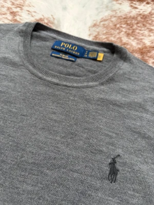 Grå Merino tröja från Polo Ralph Lauren - Klassisk grå tröja från Polo Ralph Lauren med rund halsringning och diskret broderad logga på bröstet. Tillverkad i 100% Merino och har ribbade muddar vid ärmslut och nederkant. Perfekt för en stilren look. Nypris 2400. Etiketter ingår, köpt på Ralph lauren Paris. Toppskick 9,5/10. Bara att höra av sig vid frågor//Carl