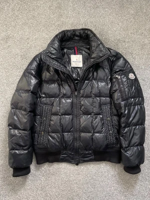 Moncler Auburn  - Moncler Auburn jacka i svart, säljes i bra skick | Sparsamt använd | Defekt på sista bild | Storlek 2 | Hör av er vid eventuella frågor eller funderingar!