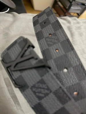 rutigt svart bälte - Snyggt svart bälte från  med klassiskt rutigt mönster. Tillverkat i skinn med beige insida och präglad märkning. Perfekt accessoar för att lyfta din outfit.