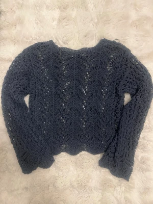 Mörkblå virkad stickad tröja - Snygg mörkblå stickad tröja med virkat mönster och lång ärm. Tröjan har en lös passform och är perfekt för lager på lager. Materialet är mjukt och luftigt, vilket gör den skön att bära. Passar till jeans eller kjol för en trendig look.