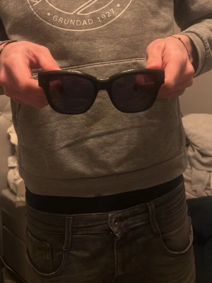 Svarta solglasögon från chimi - Säljer ett par stilrena svarta solglasögon från chimi. De har en klassisk rektangulär form och är tillverkade i blank svart plast med diskret logga på skalmen. Perfekta för dig som vill ha en clean och tidlös look.