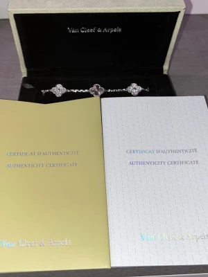 Van Cleef & Arpels Alhambra armband - Exklusivt armband från Van Cleef & Arpels Alhambra-kollektion med tre fyrklöverformade hängen, två i silver med pärldetaljer och ett i lila sten. Elegant kedja i silverfärg. Perfekt för dig som gillar lyxiga accessoarer.