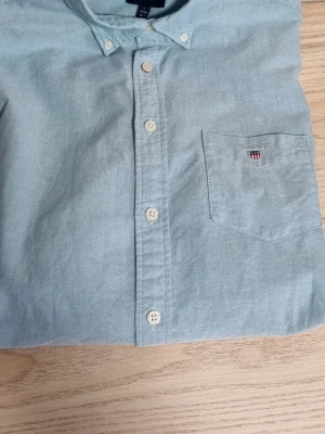 Ljusgrön/mintgrön kortärmad skjorta Gant - Snygg ljusgrön/mintgrön skjorta från Gant med korta ärmar och klassisk knappslå. Bröstficka med Gant-logga broderad ovanför. Tillverkad i mjuk bomull och har en clean, tidlös look som passar till mycket.