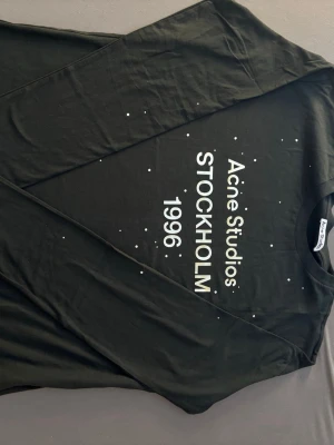 Svart Acne Studios långärmad t-shirt - Snygg svart långärmad t-shirt från Acne Studios med tryck framtill där det står 'Acne Studios STOCKHOLM 1996' och små vita prickar. Klassisk rund hals och mjukt material som känns skönt mot huden. Perfekt för dig som gillar minimalistisk och stilren design.
