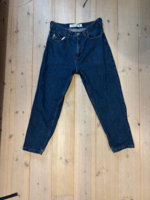 Mörkblå jeans från Polar skate Co - Säljer ett par klassiska blå jeans i modellen 92! från polar skate co med avslappnad passform. Jeansen har fem fickor, bälteshällor och en snygg vintage-vibe. Tillverkade i kraftigt denimtyg som ger en tidlös look. Säljes då jag växte ur dem nästan direkt efter att jag köpte dem.