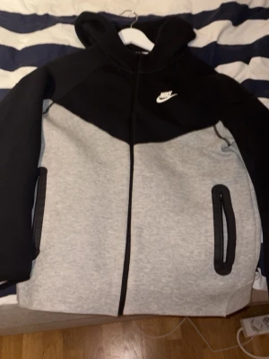 Nike tvåfärgad hoodie XL - Snygg hoodie från Nike i svart och ljusgrått med dragkedja framtill och två fickor med svarta detaljer. Klassisk Nike-logga på bröstet och huva för extra stilpoäng. Perfekt för chill dagar eller när du vill ha en sportig look.