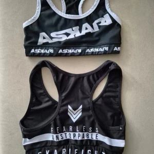 Svarta sport-bh:ar från Askari - Säljer tre olika svarta sport-bh:ar från Askari med tryckta loggor och textdetaljer. Alla har brottarrygg och bred resår under bysten. Materialet är stretchigt och snabbtorkande, perfekt för träning och gym. Snygg design med vita kontrastdetaljer.