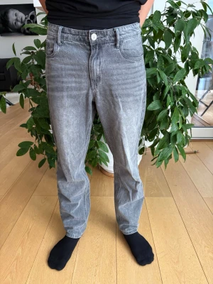 Grå tvättade raka jeans - Säljer ett par grå tvättade jeans med rak passform och klassisk femficksdesign. Jeansen har en snygg vintage-look med ljusare partier och normal midja. Perfekta för dig som gillar en avslappnad stil. Köpt på kids brands store. Storlek 14s motsvara typ 170.