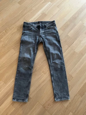 Grå tvättade slim fit jeans - Säljer ett par grå slim fit jeans med tvättad look och klassiska fem fickor. Jeansen har raka ben och normal midja. Storlek 31/32