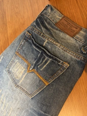Blåa flared jeans från Guess Jeans - Säljer ett par blåa baggy jeans från Guess Jeans med slitningar 