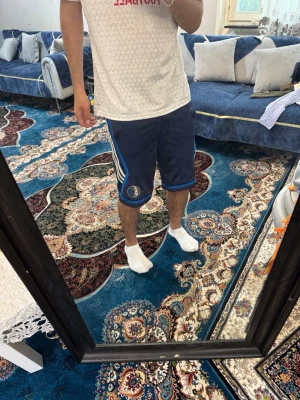 Blå basketshorts Dallas Mavericks - Säljer ett par blå basketshorts från Adidas med Dallas Mavericks-logga på vänster ben. Shortsen har vita och ljusblå ränder längs sidorna och är tillverkade i ett ventilerande meshmaterial. Perfekta för träning eller chill. 10-13 år 